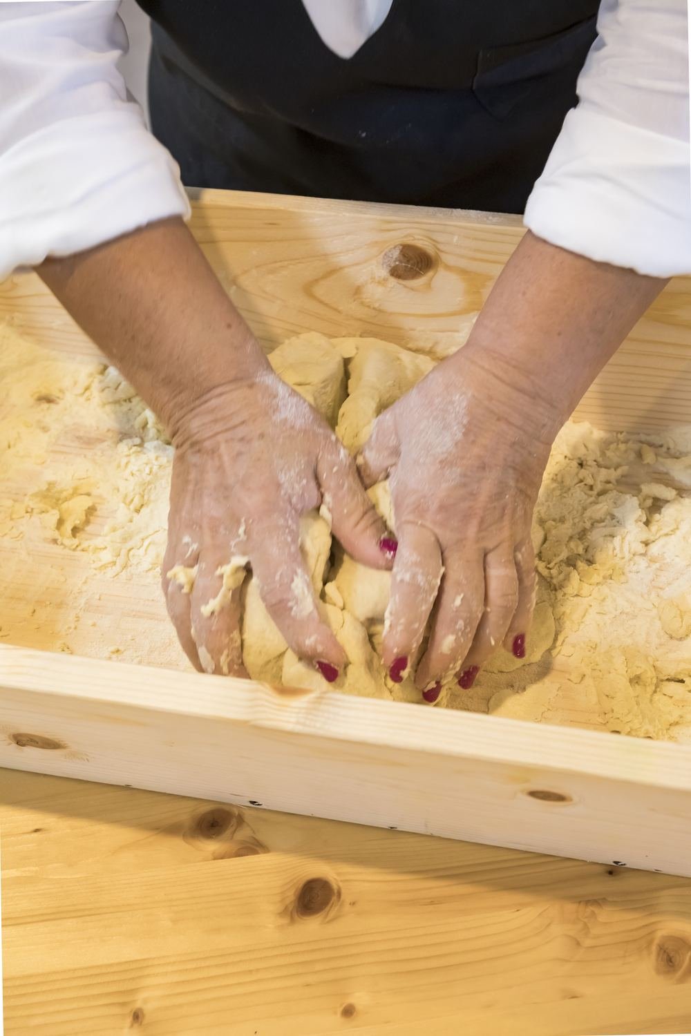 Le mani impastano semola e acqua sulla tavola di legno